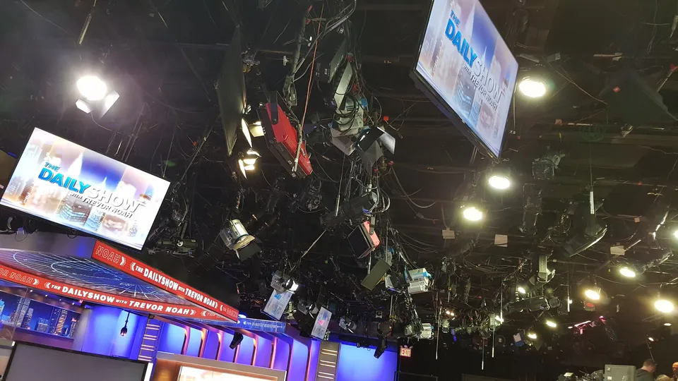 Overhead view of a television studio ceiling with cameras, lights, and screens displaying "The Daily Show" branding