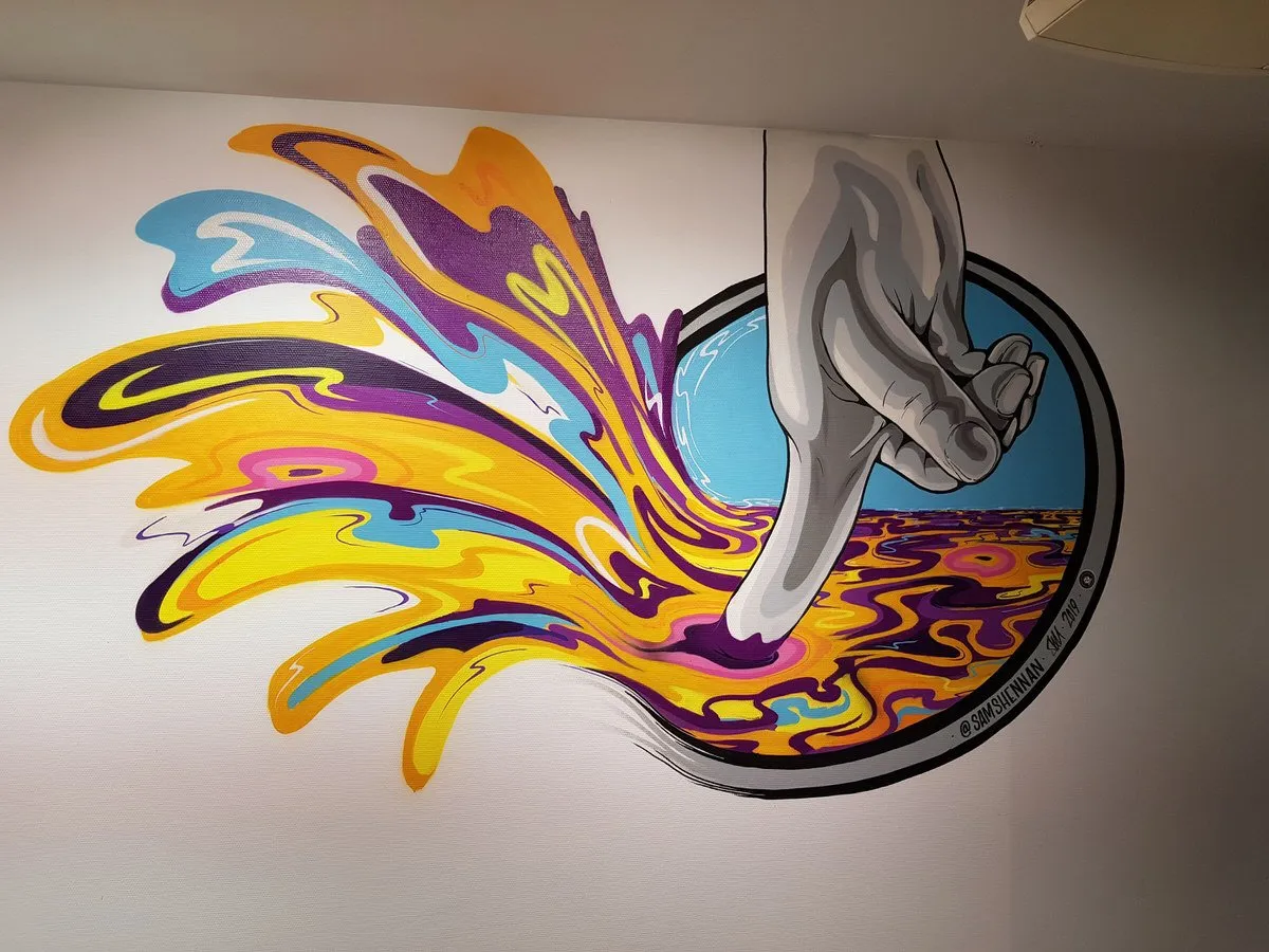 Mural of a grey hand dipping a finger into a circular portal, splashing vibrant psychedelic liquid across the wall