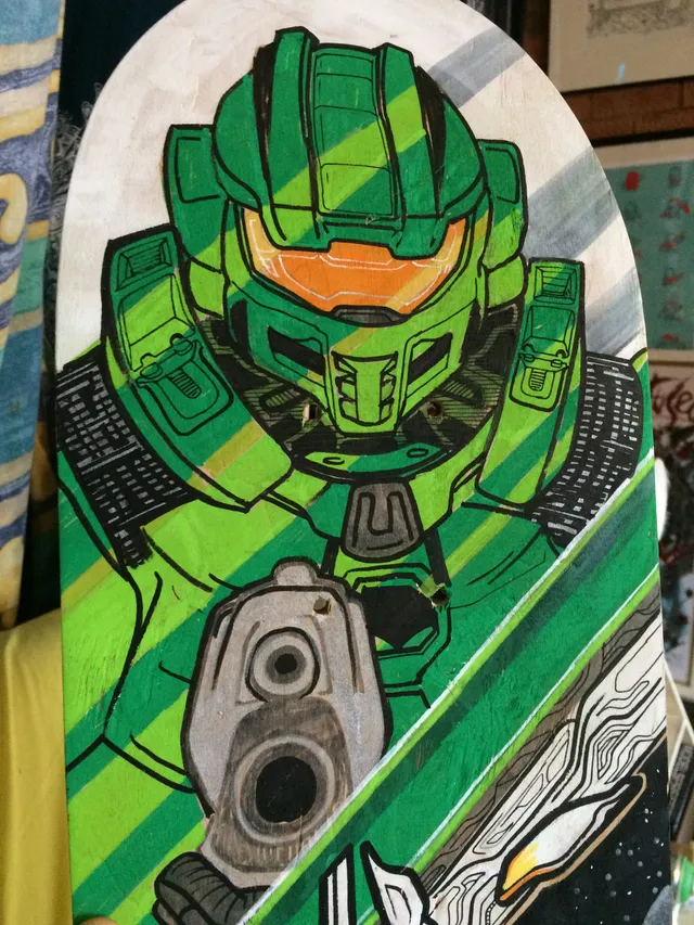 Hand-painted skateboard deck depicting a green armored sci-fi space marine aiming a pistol with bold graphic outlines