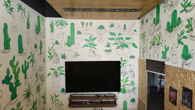 Mural of green plants and cacti growing from everyday objects drawn in black line art on white walls surrounding a TV