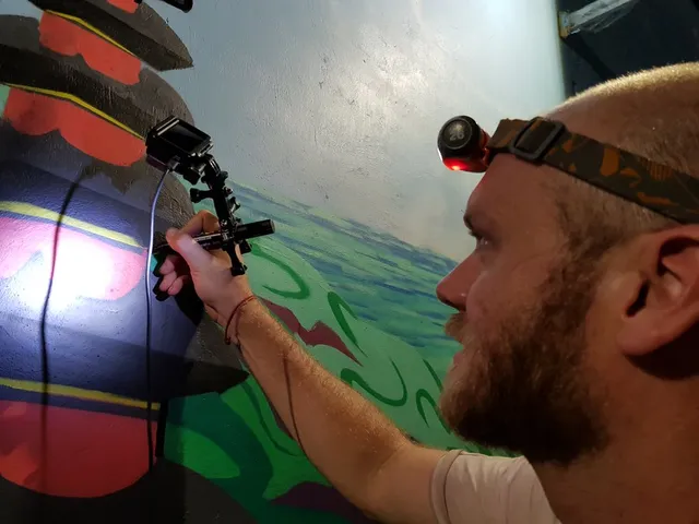 Man wearing a headlamp drawing on a colorful wall mural using a marker attached to a small action camera