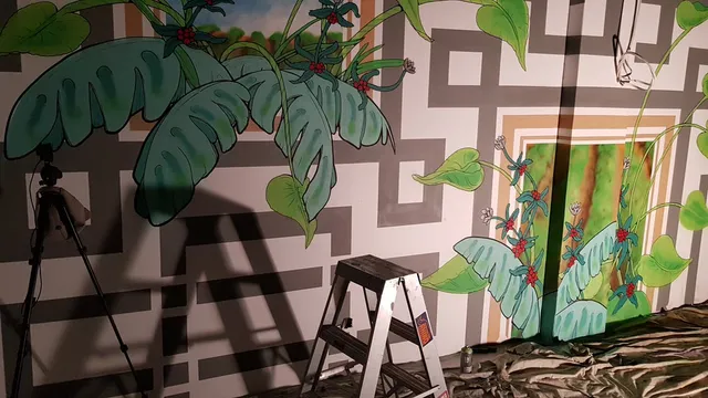 In-progress mural featuring green leaves and red coffee berries painted over a geometric grey and white background