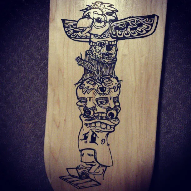 Hand-drawn black ink totem pole on a wooden skateboard deck featuring stacked animal faces and a figure using a laptop