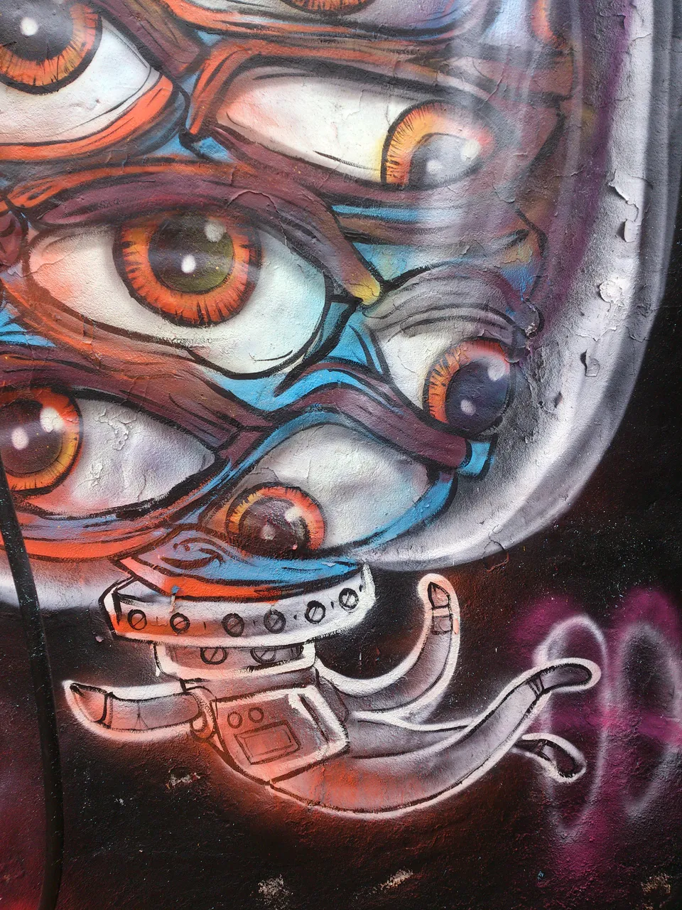 Graffiti spray paint mural of multiple orange eyes and a robotic spaceman's helmet and hand
