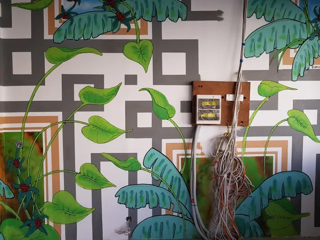Wall mural of tropical green leaves and red berries over a geometric background, painted around an exposed electrical box