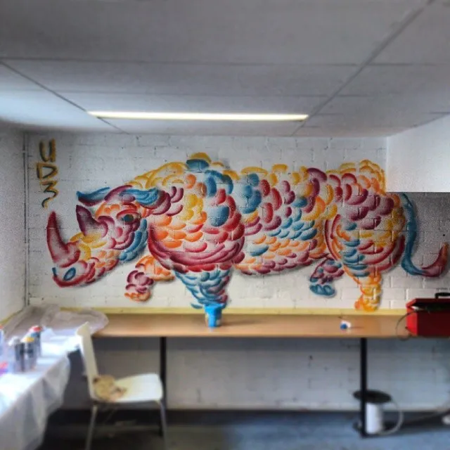 Mural on a white brick wall depicting a rhinoceros made of colorful overlapping scale patterns