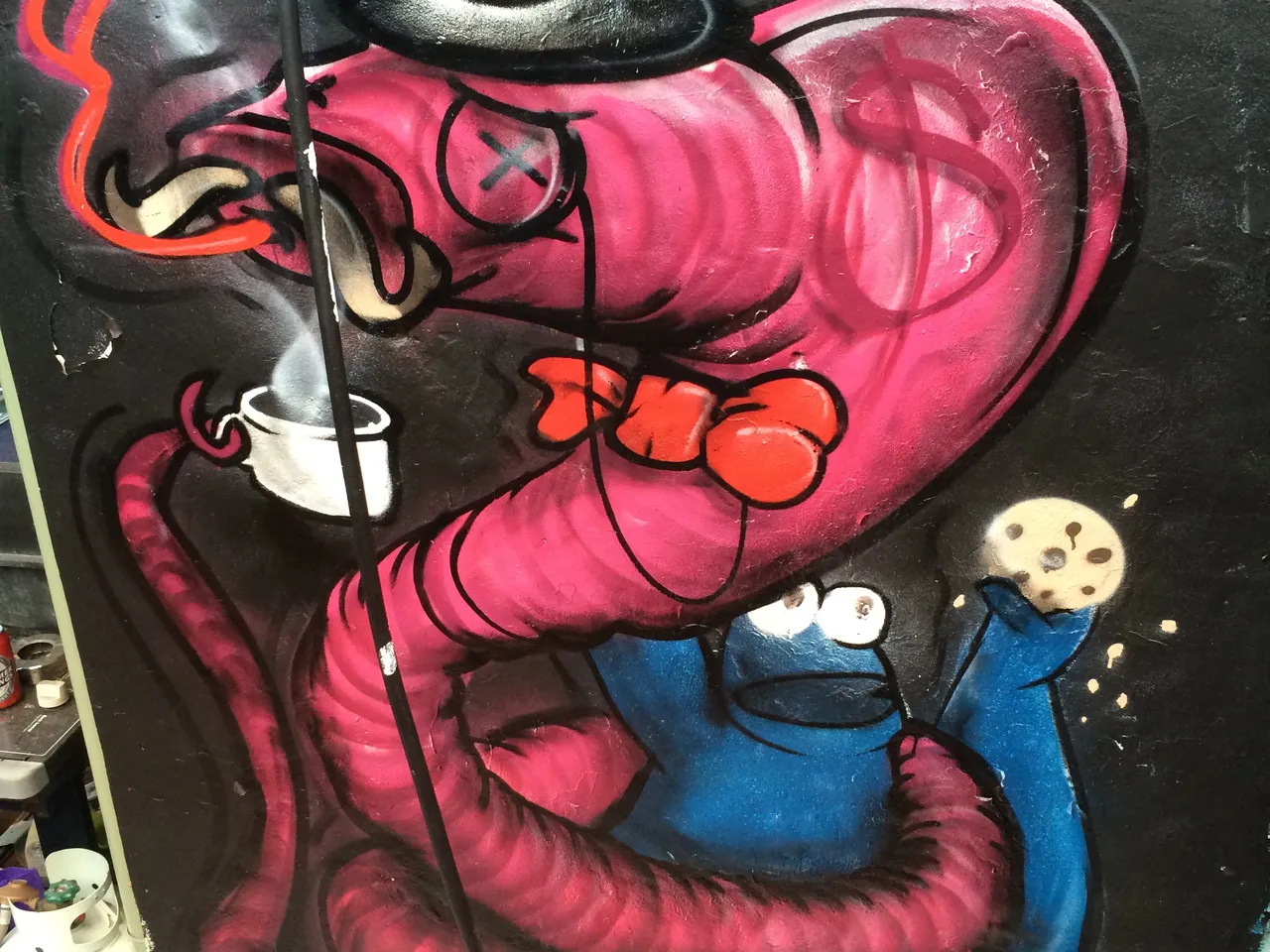 Graffiti mural: pink worm in top hat & monocle with dollar sign, constricting blue Cookie Monster holding a cookie
