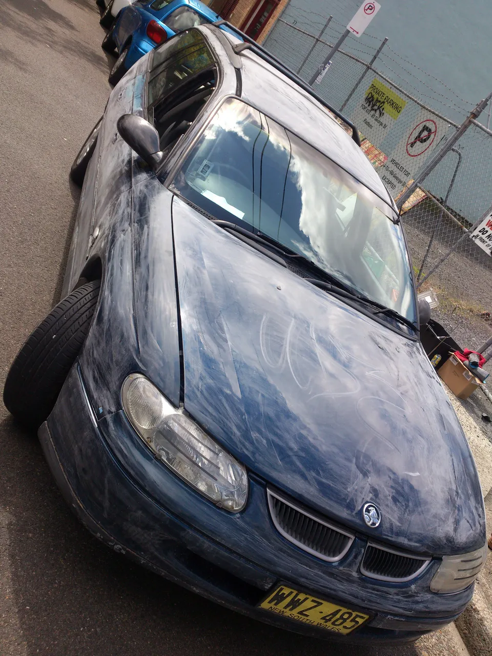 Dark blue station wagon parked on a street with its paint heavily sanded and scuffed in preparation for artwork