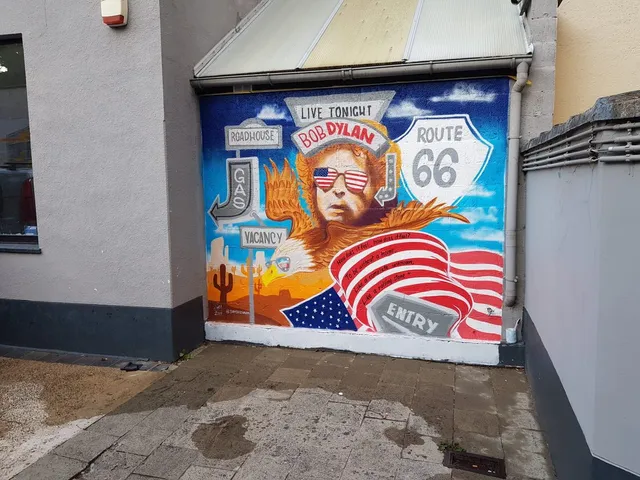 Mural of Bob Dylan wearing American flag sunglasses, an eagle, a Route 66 sign, and a desert landscape