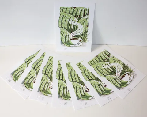 Fanned art prints showing an illustration of a steaming coffee cup surrounded by bold green jungle leaves