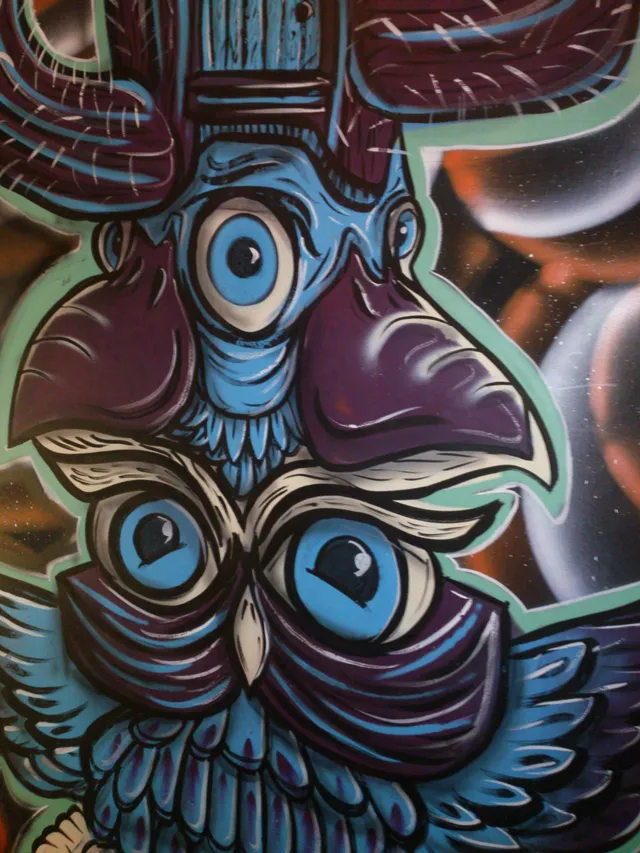 Detail of a painted psychedelic totem featuring a blue owl and a one-eyed creature against a cosmic background
