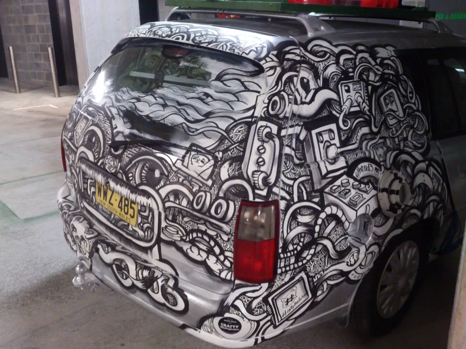 Silver car hand-painted with dense black and white line art of intertwining tubes, electrical plugs, and large eyes