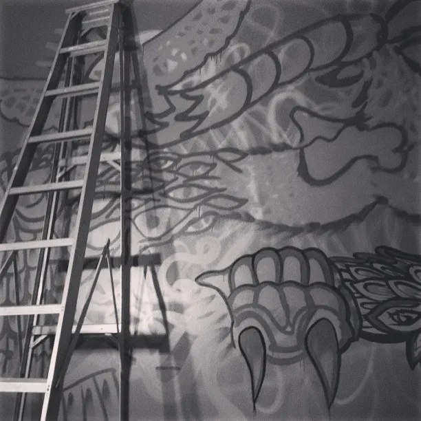 Tall stepladder in front of an unfinished mural featuring bold outlines of a totemic creature with large claws