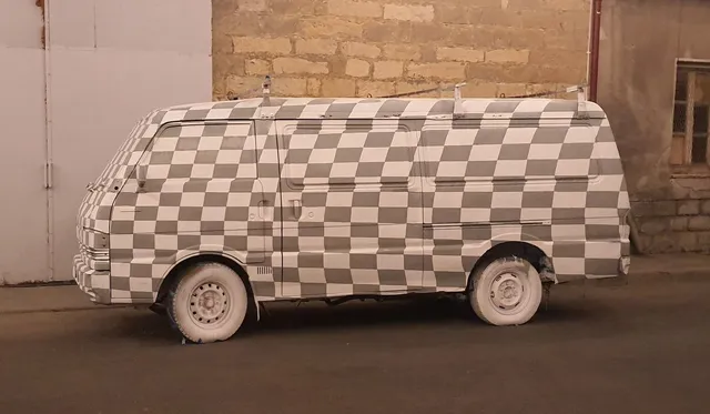 Van painted entirely in a grey and white checkerboard pattern including windows, with solid white wheels and tires