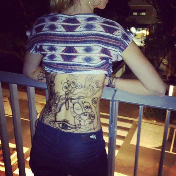 Psychedelic black ink drawing of multiple eyes and organic shapes on a woman's back