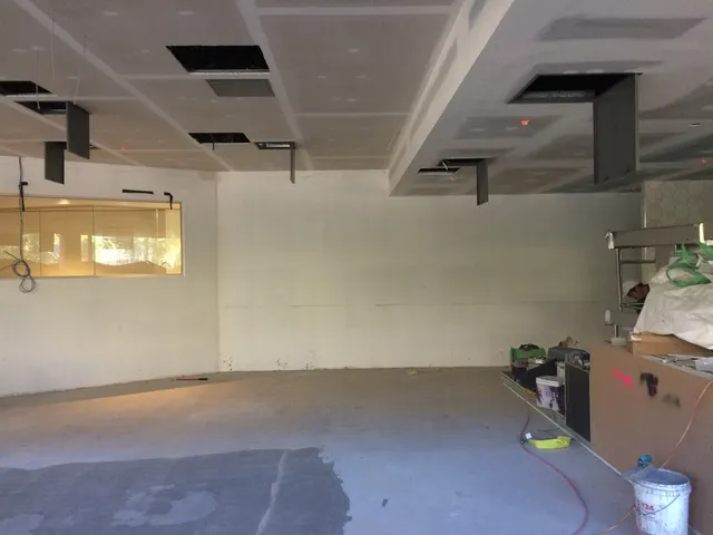 Blank white wall in an unfinished room with an exposed ceiling and painting supplies