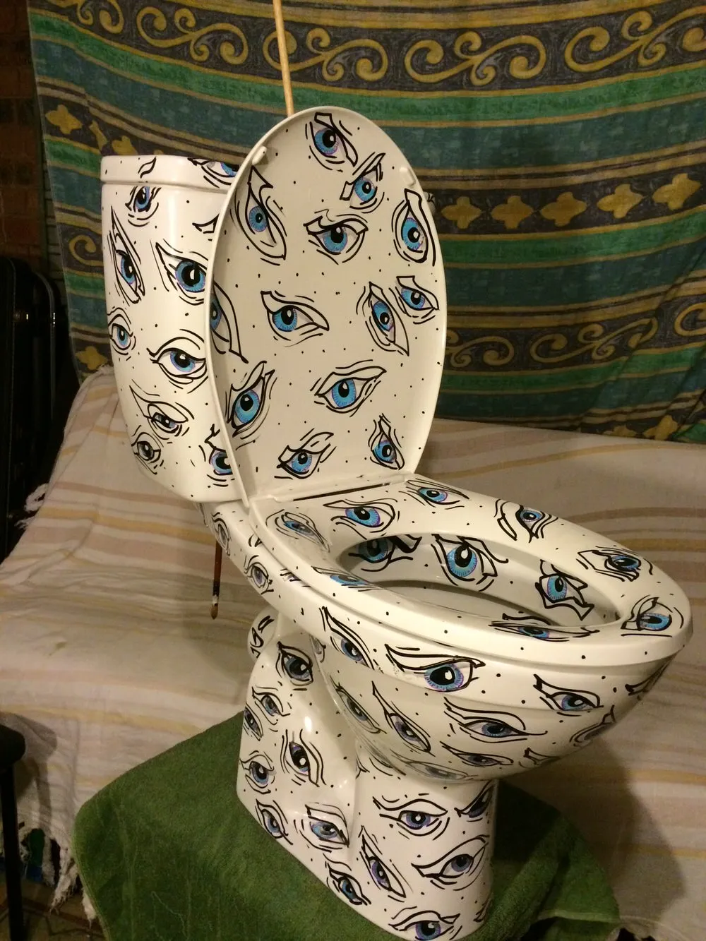 Hand-painted toilet covered in a repeating pattern of stylized blue eyes with bold black outlines