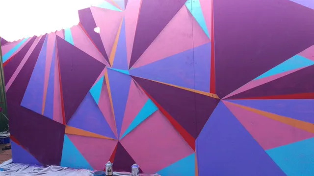 In-progress abstract mural of geometric pink, purple, and blue triangles with spray paint cans on a drop cloth