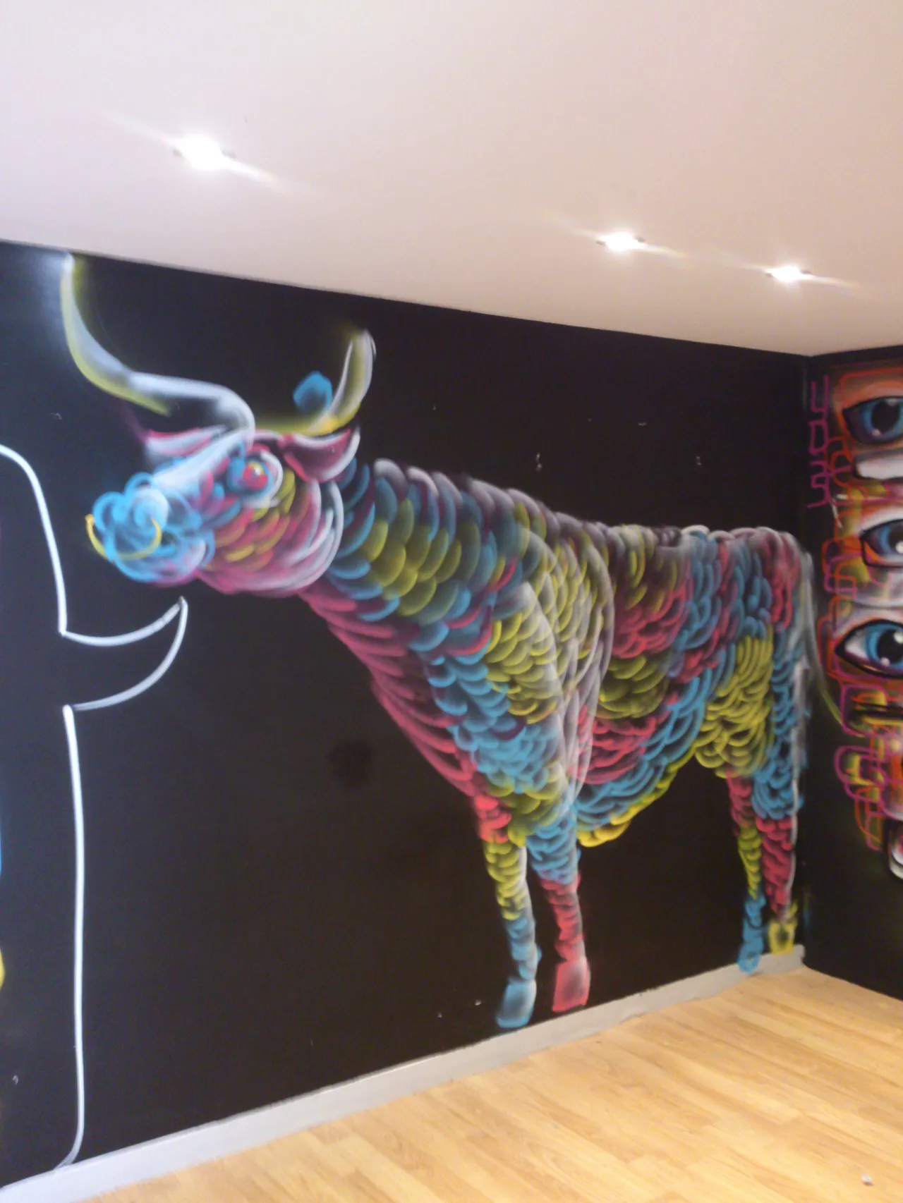 Mural of a colorful psychedelic bull composed of overlapping curved strokes on a black wall