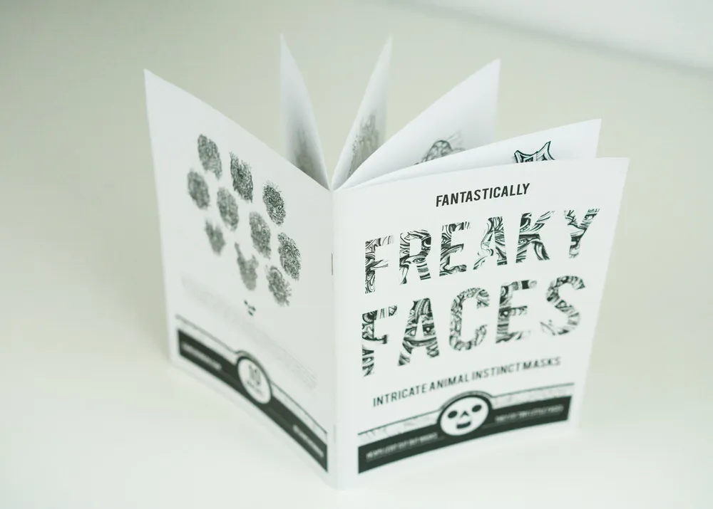 Printed zine titled Fantastically Freaky Faces standing open with fanned pages showing black and white illustrations