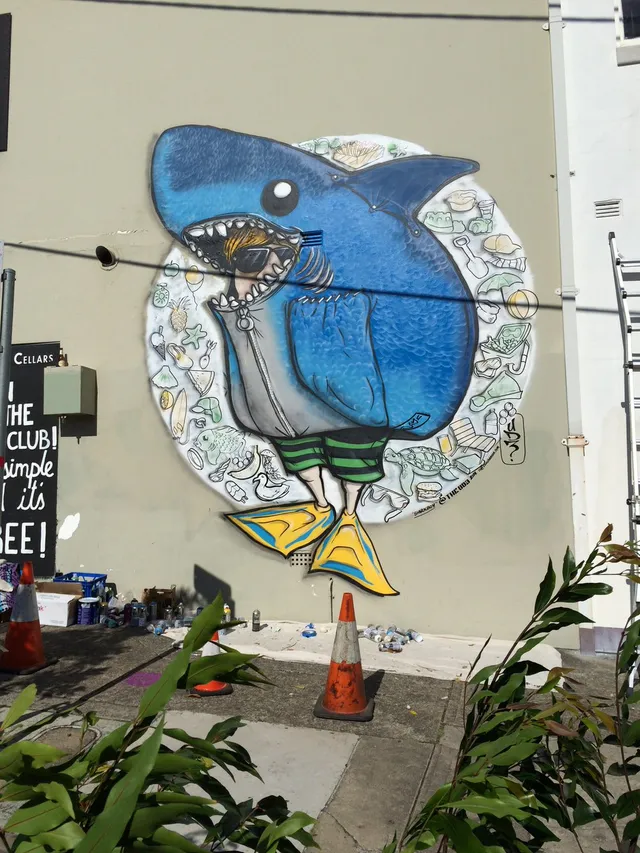 Mural of a boy in a blue shark costume, striped shorts and yellow flippers surrounded by a halo of beach-themed line art