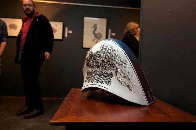 Hand-painted white helmet on a gallery table featuring a black line drawing of a totemic dog head and the word ROBDOG