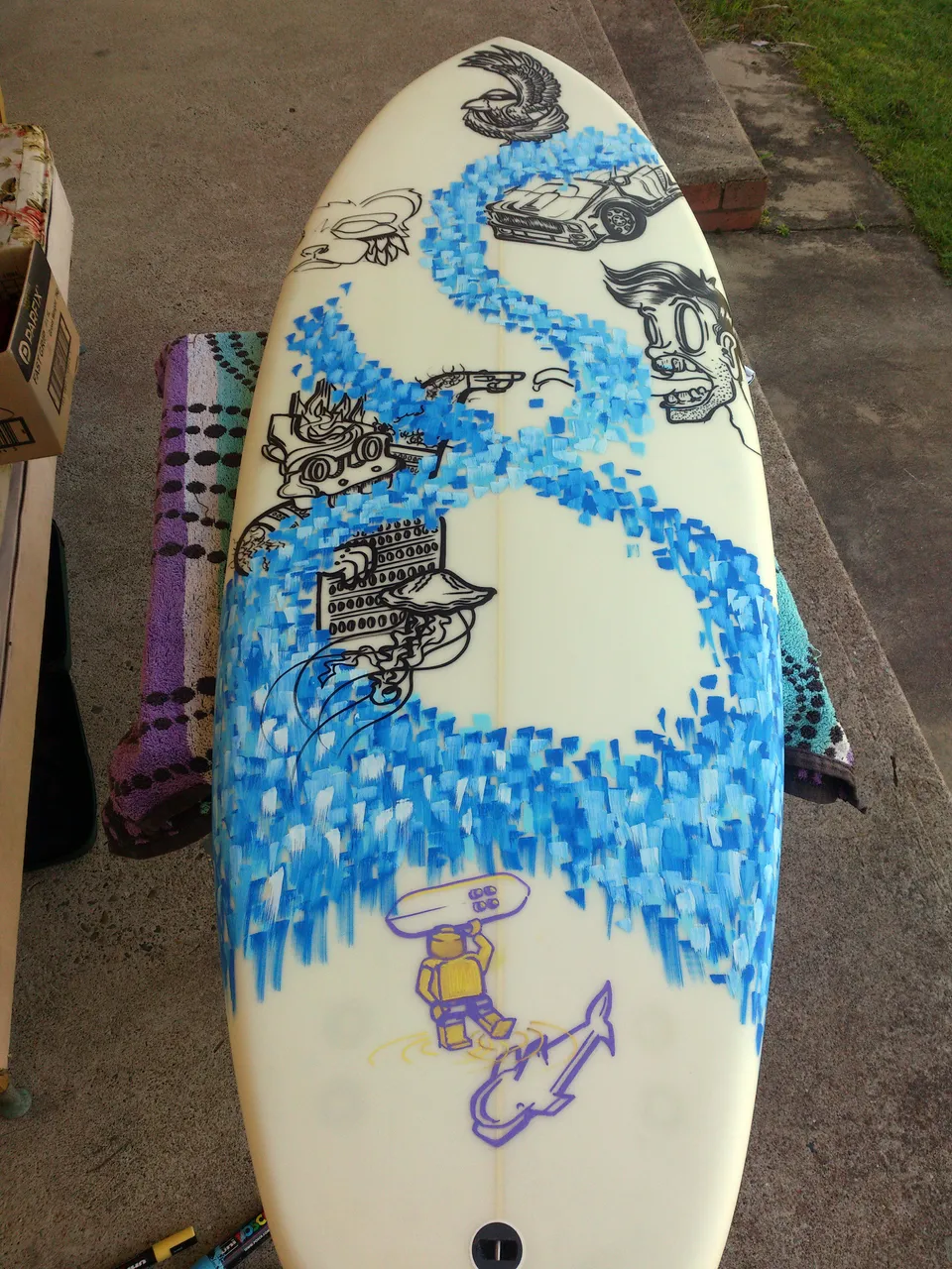 Painted surfboard with black line art of various figures and objects intertwined with a swirling blue wave pattern