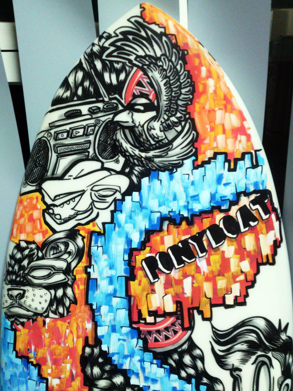 Painted surfboard featuring black and white animal masks and a boombox amidst blocky blue and orange patterns