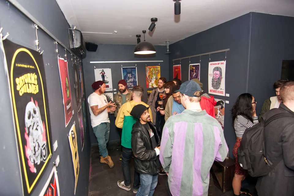 Crowd mingling at a gallery exhibition with colorful illustrated posters hanging on dark walls