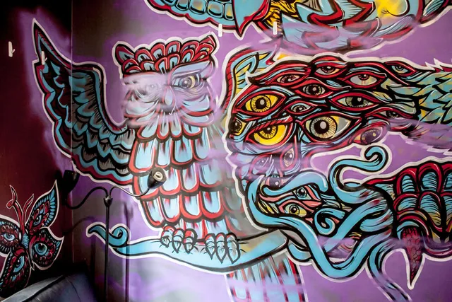 Psychedelic mural of a blue and red owl with a wing made of staring eyes painted on a purple wall