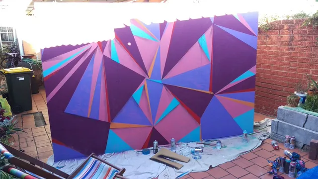 Large freestanding panel painted with a faceted geometric mural in shades of purple, pink, and blue spray paint" (109