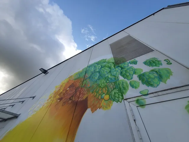 Mural on a white building featuring a stylized wave of green hops transitioning into golden liquid