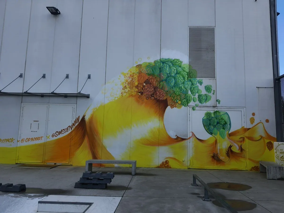 Mural on a white wall depicting a crashing wave of golden liquid cresting into green hops