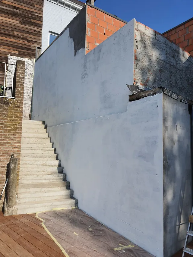 Blank white primed exterior wall next to concrete stairs, prepared for a mural with drop cloths on the wooden deck