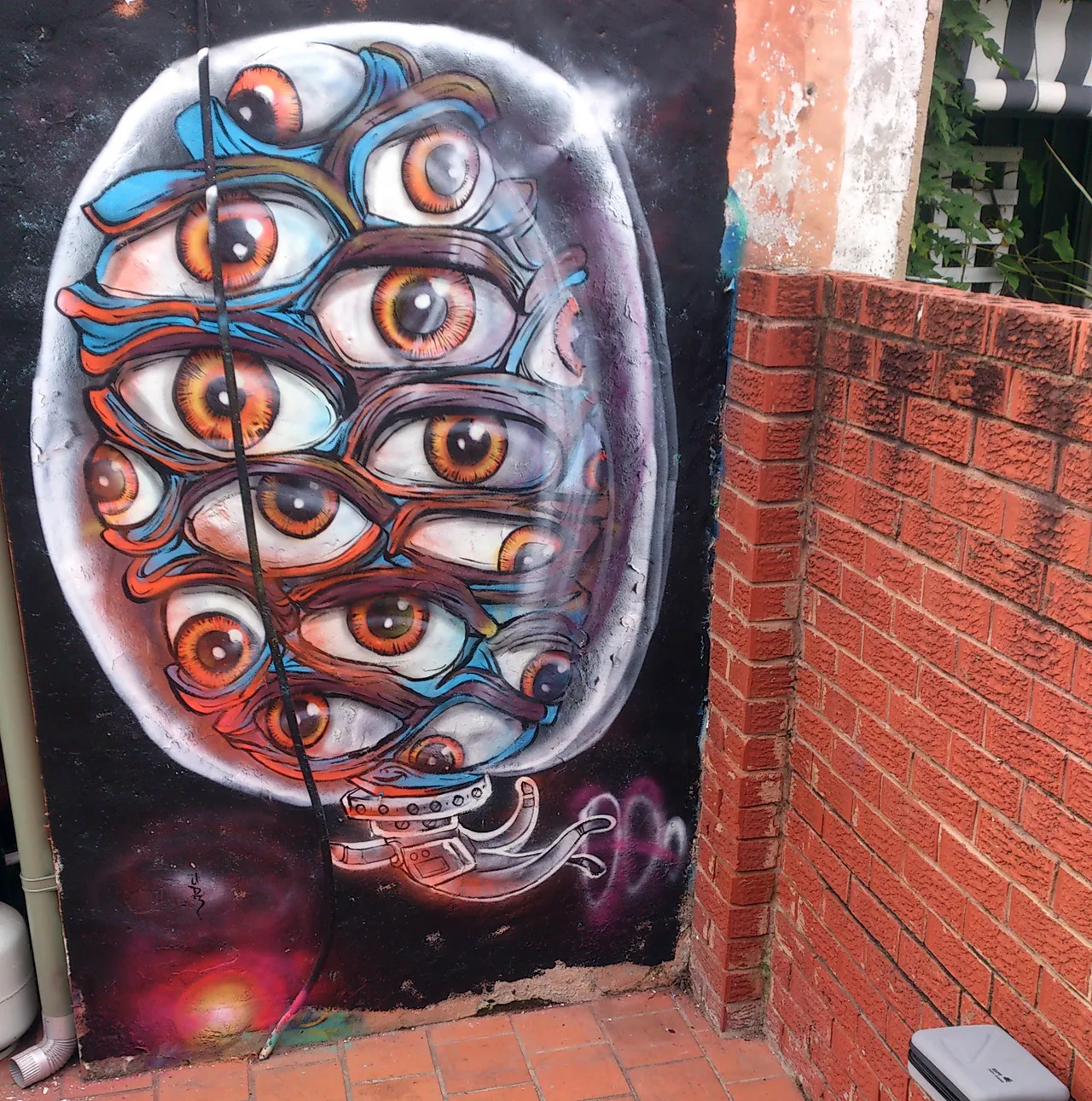 Psychedelic mural of a dense oval cluster of overlapping orange eyes attached to a mechanical base
