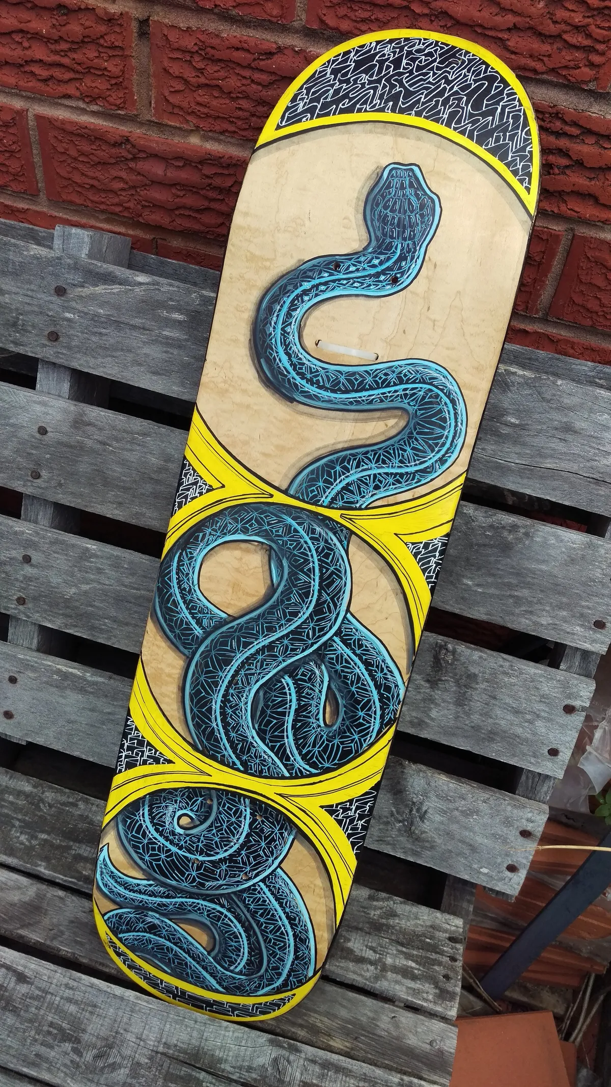 Hand-painted skateboard featuring a coiled blue snake with intricate linework and bold yellow accents on natural wood