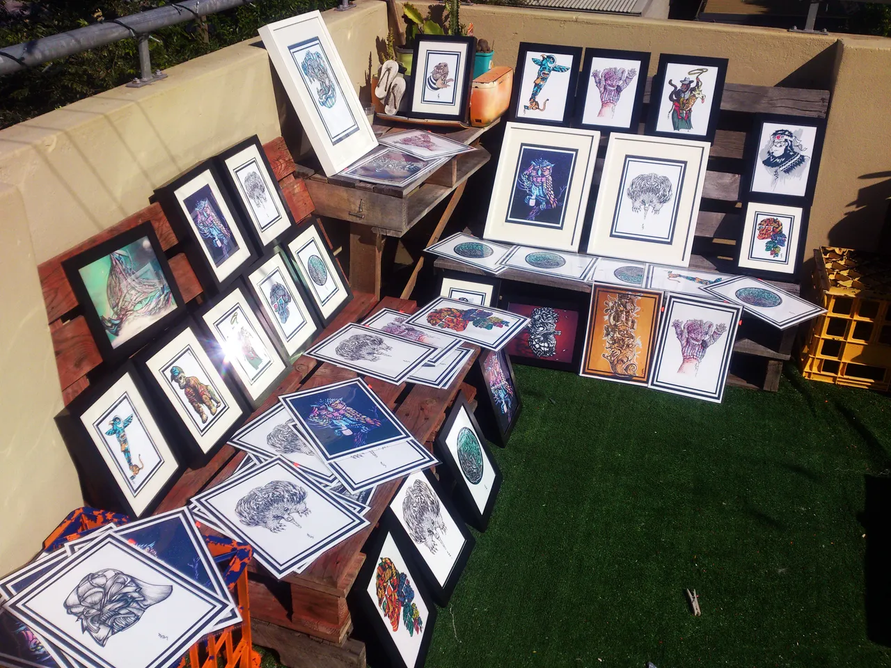 Collection of framed and unframed psychedelic illustration prints displayed outdoors on wooden pallets