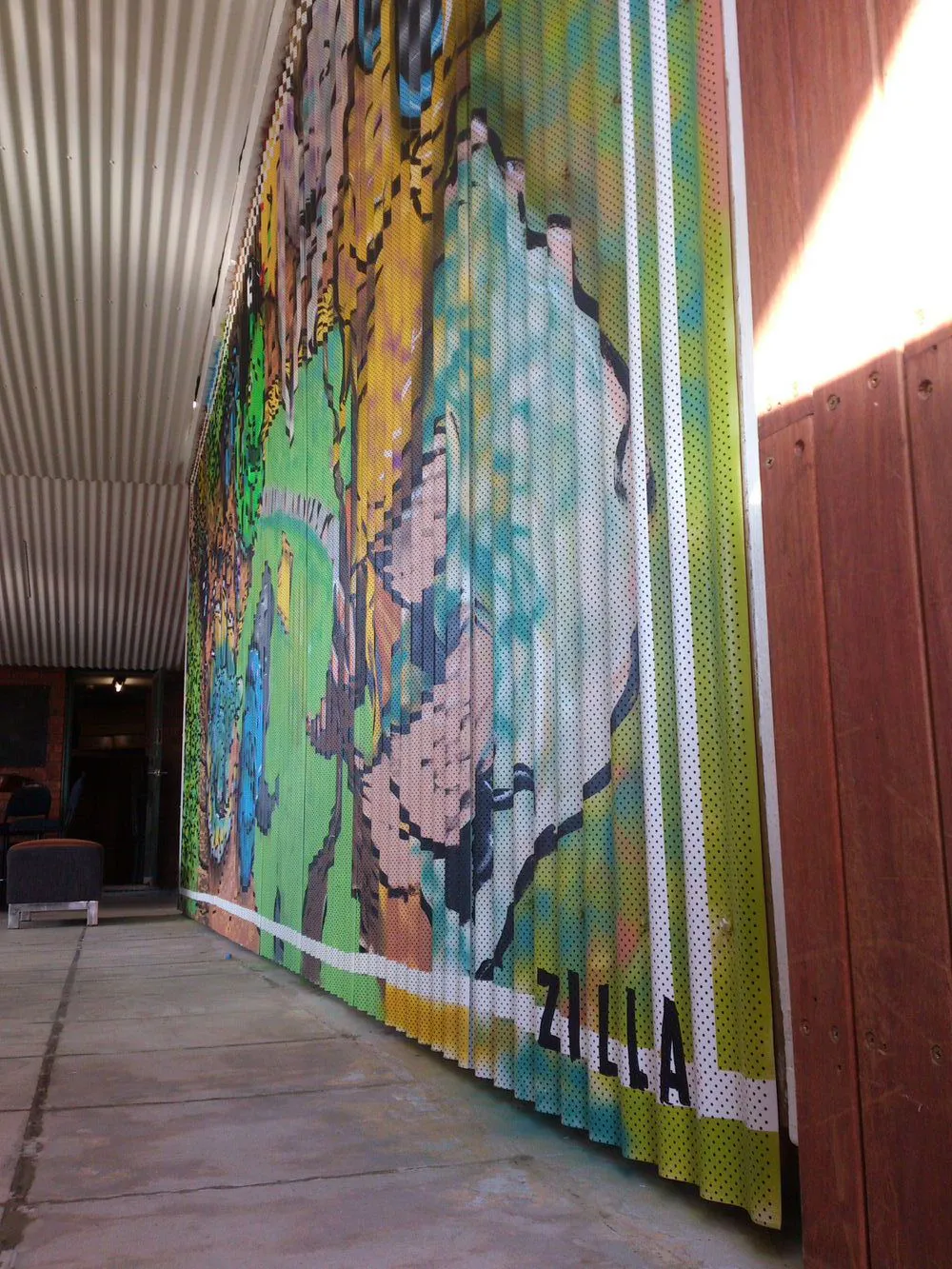 Colorful mural painted on a corrugated metal wall featuring bold shapes, dotted patterns, and the word ZILLA