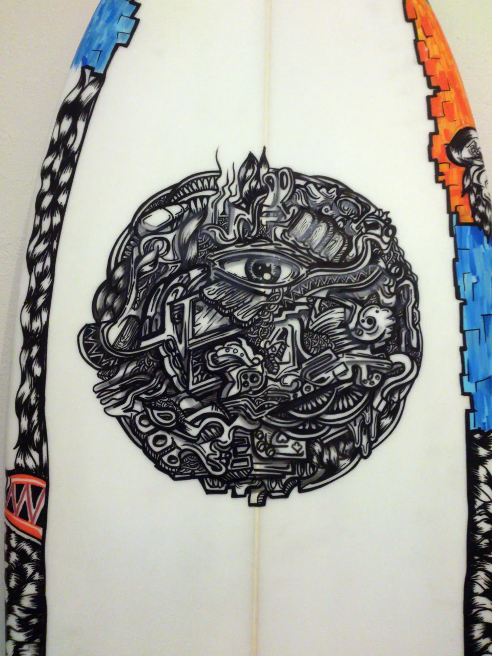 Painted surfboard with a central black and white circular illustration of an eye amidst intricate psychedelic shapes