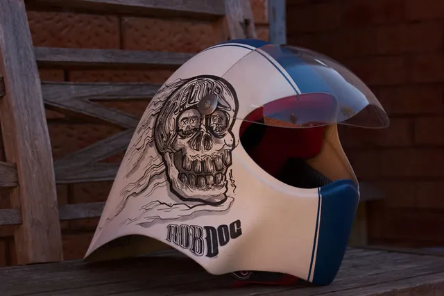 White helmet with a blue stripe, hand-painted with a bold black line skull illustration and the text ROB DOG