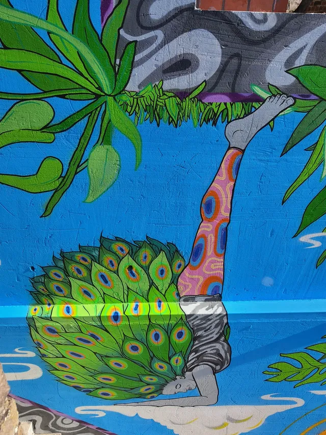 Mural of a person in an inverted yoga pose with patterned leggings and a large fan of peacock feathers on their back