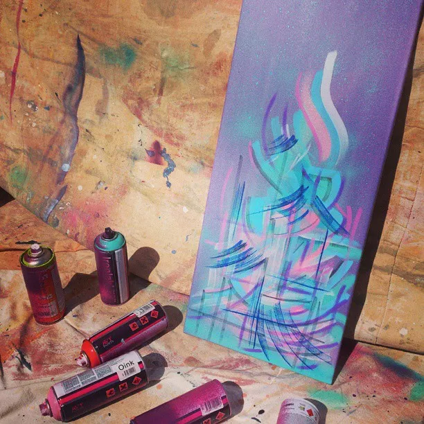 Abstract spray painting of sweeping teal, pink, and purple lines on a tall canvas surrounded by spray cans