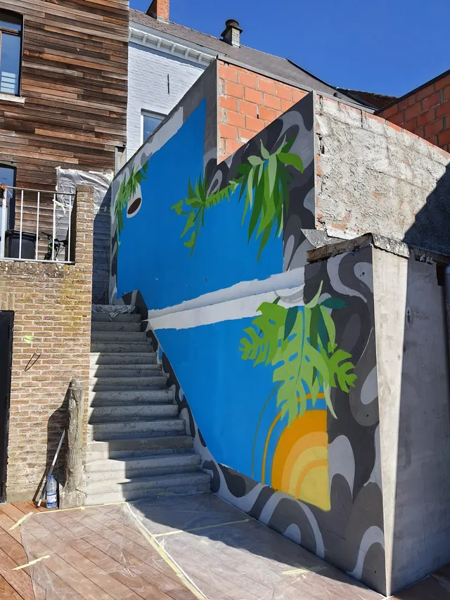 In-progress outdoor mural next to stairs featuring bright blue panels, green tropical leaves and a yellow sun