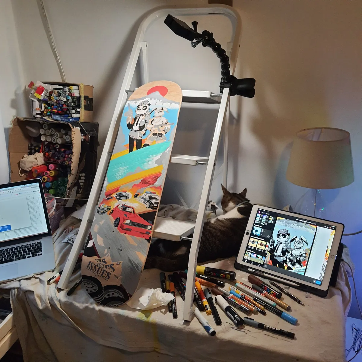 Hand-painted skateboard depicting armed animal characters and a car chase, leaning in a studio space among paint markers