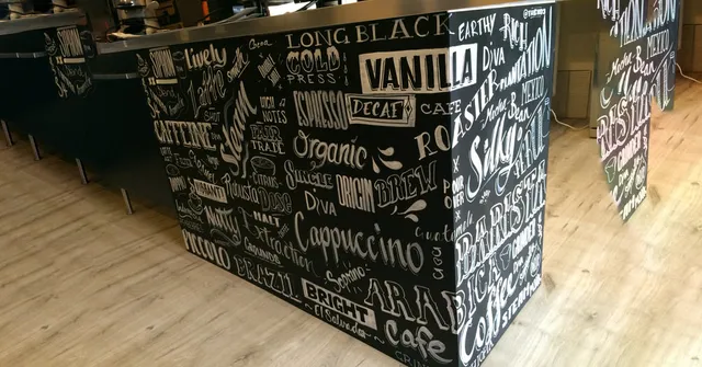 Hand-painted white lettering on a black cafe counter featuring various coffee terms in diverse styles