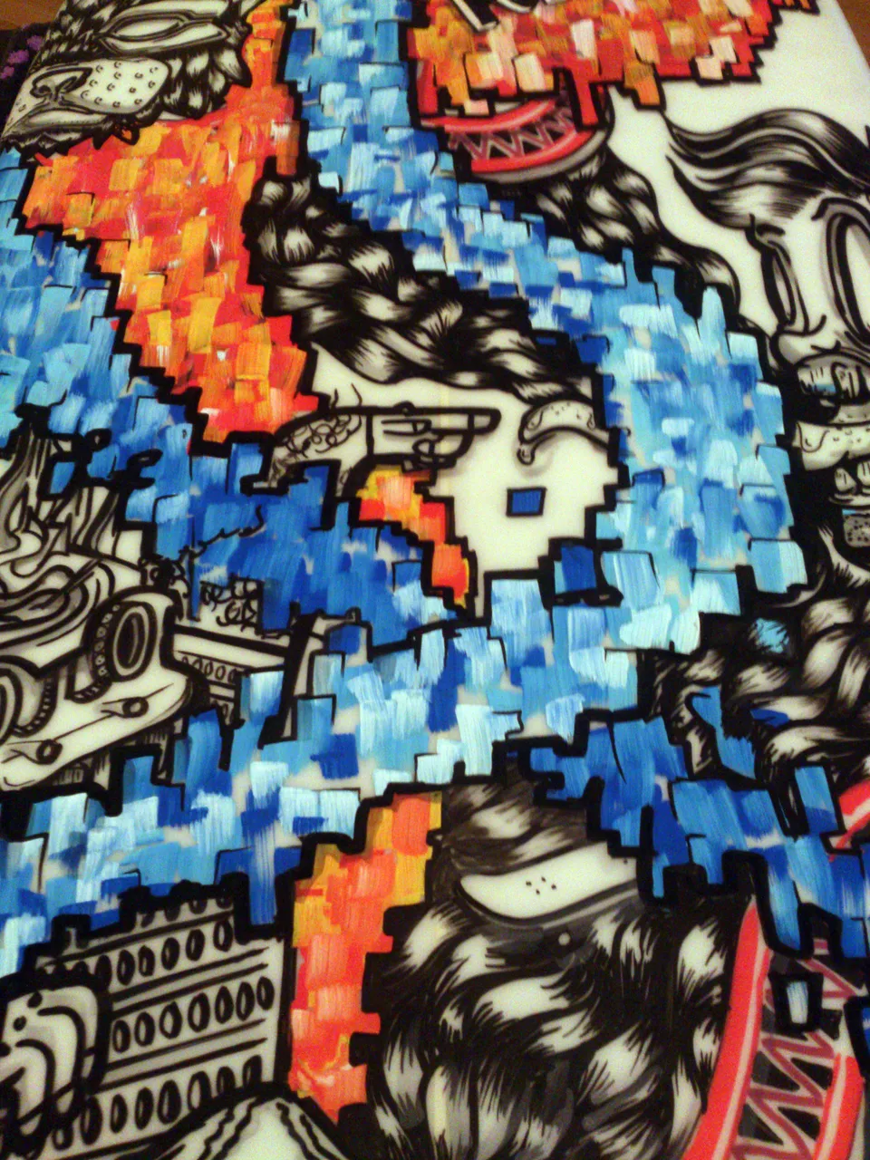 Painted surfboard detail combining black and white line art faces with jagged, pixelated blocks of blue and orange paint