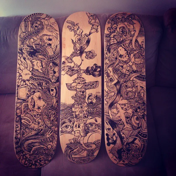 Three wooden skateboard decks featuring intricate black ink drawings of psychedelic faces, eyes and totemic creatures