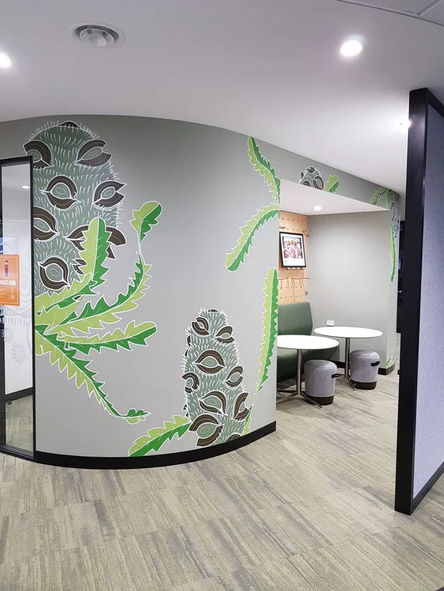 Stylized botanical mural featuring large textured seed pods and jagged green leaves on a curved office wall