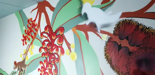 In-progress wall mural featuring vibrant red Australian native flowers, a small marsupial and a white bird silhouette
