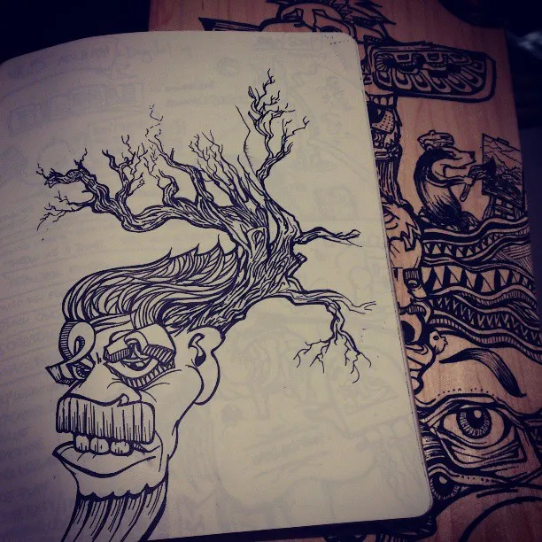 Ink sketch of a surreal face with hair growing into a bare tree, resting on a wooden surface covered in totemic line art